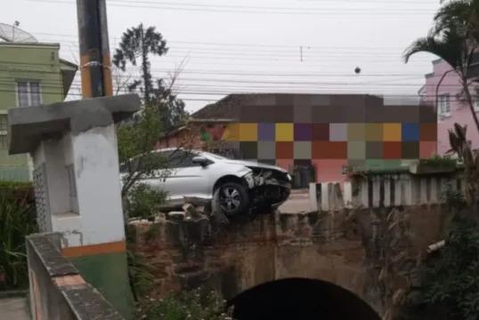 Motorista perde o controle do veículo e acaba pendurado em mureta de proteção em um ribeirão